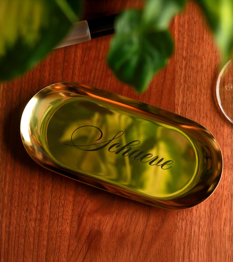 Silver metal oval trinket tray on light tabletop, modern minimalist design used as jewelry dish and vanity organizer.