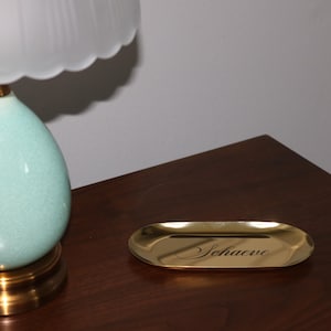 Lifestyle shot of gold trinket tray on white cloth with jewelry and accessories, minimalist modern look.