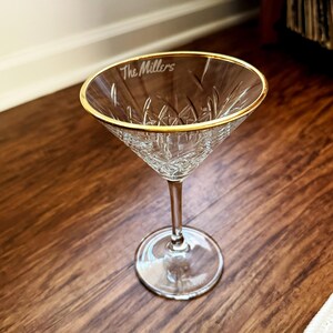 Op de afbeelding: Een helder martiniglas met een gouden rand en een ge&euml;tst diamantpatroon. De tekst "The Millers" is op de rand ge&euml;tst. Het glas staat op een houten oppervlak.