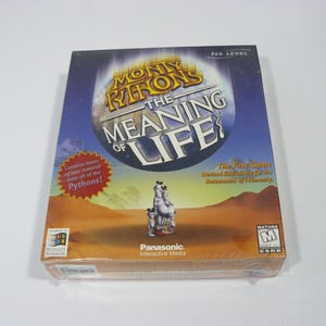 May include: A computer game box cover featuring a cartoon image of a group of people standing on a desert landscape. The title of the game is "Monty Python's The Meaning of Life?" and the box is labeled "The First Game Designed Exclusively for the Department of Humanity".