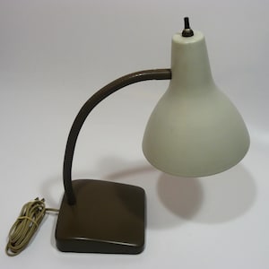 May include: A vintage desk lamp with a cream-colored shade and a dark brown, flexible arm. The base is a matching dark brown square. The lamp has a cord with a plug.