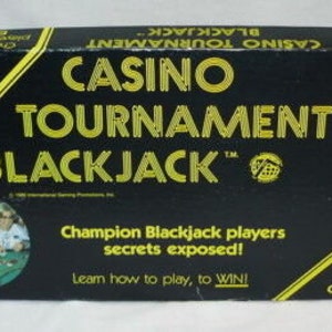 May include: A black and yellow game box for Casino Tournament Blackjack. The box features a photo of people playing the game and the text "Champion Blackjack players secrets exposed! Learn how to play, to WIN!"