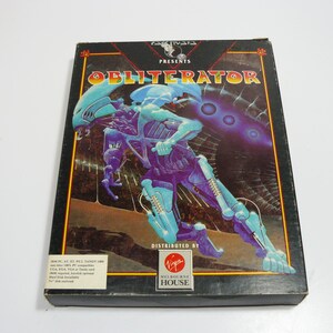 May include: A vintage video game box for "Obliterator" featuring a futuristic alien warrior in shades of blue and purple. The box has a black background with gold trim and the Virgin Games logo.