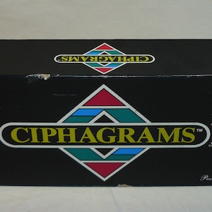 May include: A black box with the word "CIPHAGRAMS" in yellow letters on a green, blue, red, and white diamond shape. The box is labeled "Premiere Edition" and has a small red sticker on the top right corner.