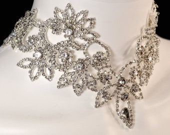 May include: A silver rhinestone choker necklace with a floral design. The necklace is made of small, clear rhinestones that are set in a delicate, intricate pattern.