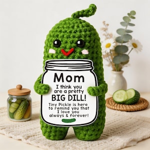 Puede incluir: Una figura de pepinillo de ganchillo verde hecha a mano que sostiene un letrero que dice "¡Mamá, creo que eres un pepinillo bastante GRANDE!" El letrero también dice "¡Tiny Pickle está aquí para recordarte que te amo siempre y para siempre!" Un tarro de pepinillos está en el fondo.