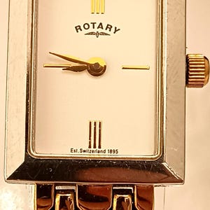 May include: A rectangular Rotary watch with a silver and gold-tone bracelet and case. The white watch face has gold hands and markers, the Rotary logo and "Est. Switzerland 1895" text.
