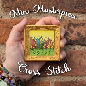 May include: A square cross stitch artwork featuring five colorful dancing figures in a pixelated style, set against a yellow and green background. The piece is encased in an ornate, metallic gold-colored frame with intricate relief detailing.