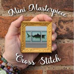 May include: A small, gold-framed cross-stitch featuring a shark in an aquarium setting. The artwork is labeled "Mini Masterpiece Cross Stitch" in elegant script. The frame has ornate detailing, and the background is a brick wall.