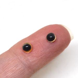 May include: Two black and orange glass eyes for crafts. The eyes are small and round, with a black pupil and an orange iris.