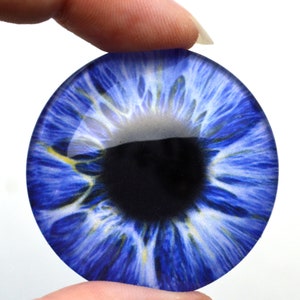May include: A close-up of a blue glass eye with a black pupil and white iris. The eye has a detailed design with blue and white streaks.