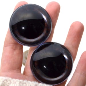 Puede incluir: Dos ojos de seguridad de plástico negro y marrón con un acabado brillante. Los ojos son redondos y tienen una pupila negra.