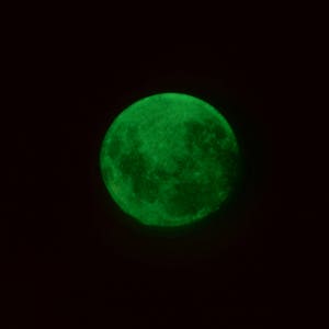 May include: A full moon glowing green in a dark night sky.