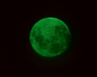 May include: A full moon glowing green in a dark night sky.
