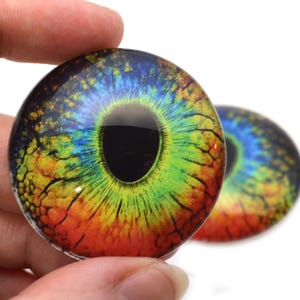 May include: Two colorful glass eyes with a rainbow iris and black pupil. The eyes have a textured surface and are perfect for crafting projects.