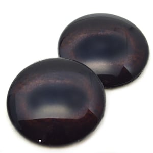 Puede incluir: Dos ojos de vidrio negros y marrones con un iris marrón oscuro y un anillo exterior marrón claro. Los ojos son redondos y tienen un acabado brillante.