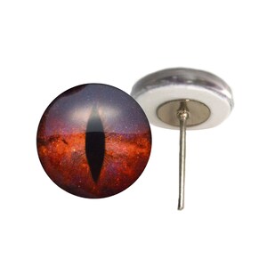 May include: A red and purple glass eye with a black pupil, mounted on a silver pin. The eye has a galaxy-like pattern.