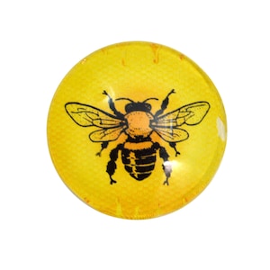 May include: A round, yellow glass paperweight with a black and orange bee illustration.