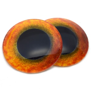 Op de afbeelding: Twee ronde, oranje, gele en zwarte plastic ogen met een zwarte pupil. De ogen zijn voor knutselen en hebben een diameter van ongeveer 2,5 cm.