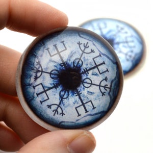 May include: A pair of blue glass eyes with a black center and a white background. The eyes have a compass design with runes around the center.