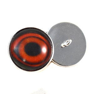 May include: A red and black eye button with a silver rim. The button has a black back with a silver loop for sewing.