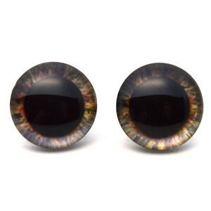 Pode incluir: Dois olhos de segurança de plástico marrom e preto com uma pupila preta e um anel marrom ao redor da pupila. Os olhos têm um padrão marrom e preto manchado ao redor da borda externa.