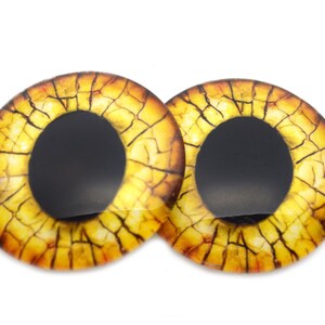 May include: Two round, glass eye cabochons with a yellow and brown cracked pattern. The irises are yellow with brown cracks, and the pupils are black. These craft supplies are ideal for doll making or jewelry.