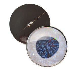 May include: A pair of round buttons with a silver metal rim. One button is black and the other has a white background with blue glitter and a silver metal rim.
