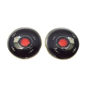 May include: A pair of black and silver round glass eyes with a red center. The eyes have a metallic rim and a design of concentric circles around the red center.