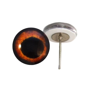 May include: A pair of glass eye cabochons with a realistic design. One eye is shown with a dark brown iris and a black pupil. The other eye has a metal pin attached to the back. The eyes are for crafts.