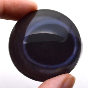 Peut inclure: Une pierre d'obsidienne ronde et noire avec un reflet bleu irisé. La pierre est lisse et polie.