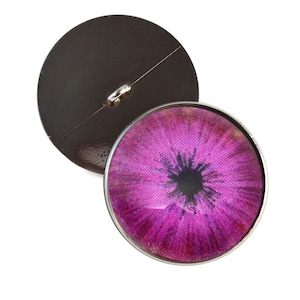 May include: A pink eye button with a black pupil and a silver rim. The back of the button is brown.