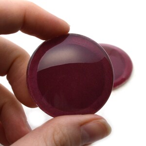 Op de afbeelding: Twee ronde, bordeauxrode glazen cabochons met een glanzende afwerking. De cabochons zijn licht gewelfd en hebben een glad, gepolijst oppervlak.