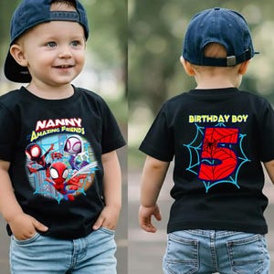K&ouml;nnte beinhalten: Schwarzes T-Shirt mit Spider-Man und anderen Charakteren und dem Text "Nanny Amazing Friends" auf der Vorderseite. Auf der R&uuml;ckseite des T-Shirts steht "Birthday Boy" und eine gro&szlig;e 5 in einem Spinnennetz-Design. Das Kind tr&auml;gt eine blaue Baseballkappe.