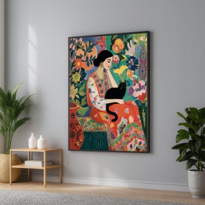 Könnte beinhalten: Ein gerahmter Wandkunstdruck, der eine Person mit dunklem Haar in einem gemusterten orange-weißen Gewand zeigt, die inmitten von leuchtenden Blumen und Blättern sitzt und eine schwarze Katze hält. Das Kunstwerk besticht durch eine reiche Farbpalette.