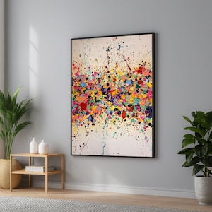 Op de afbeelding: Een rechthoekig wandkunstwerk in een zwarte lijst met een gebroken witte achtergrond bedekt met een dichte, horizontale band van veelkleurige verfspatten, waaronder tinten rood, geel, blauw, groen, roze en paarse stippen en strepen.