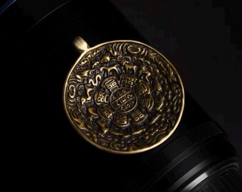 Könnte beinhalten: Ein detaillierter, antiker Bronzeanhänger mit einem komplizierten geprägten Design. Der Anhänger zeigt ein zentrales Blumenmuster, umgeben von Symbolen und Tierfiguren. Er hat eine kleine Schlaufe zum Aufhängen und ist vor dunklem Hintergrund platziert.