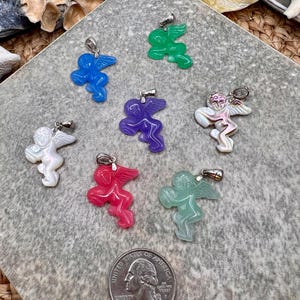 Puede incluir: Una colecci&oacute;n de colgantes de &aacute;ngeles coloridos en azul, verde, morado, blanco, rojo y verde claro. Cada colgante presenta un dise&ntilde;o detallado de &aacute;ngel con alas y una argolla plateada para colgar. Se incluye una moneda de 25 centavos de EE. UU. como referencia de tama&ntilde;o.