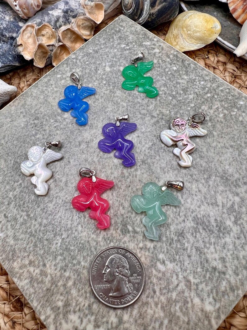 Puede incluir: Una colecci&oacute;n de colgantes de &aacute;ngeles coloridos en azul, verde, morado, blanco, rojo y verde claro. Cada colgante presenta un dise&ntilde;o detallado de &aacute;ngel con alas y una argolla plateada para colgar. Se incluye una moneda de 25 centavos de EE. UU. como referencia de tama&ntilde;o.