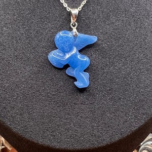 Puede incluir: Collar con colgante azul oc&eacute;ano con un &aacute;ngel tallado. El &aacute;ngel tiene alas extendidas y est&aacute; suspendido de una delicada cadena plateada. El colgante es de color azul vibrante. El texto "OCEAN BLUE" est&aacute; en la parte inferior.