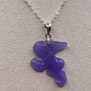 Puede incluir: Collar con colgante lavanda con dise&ntilde;o de &aacute;ngel. El colgante cuelga de una fina cadena plateada. El texto "LAVENDER DREAM" se muestra en la parte inferior de la imagen.