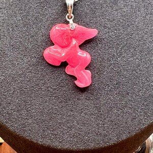 Puede incluir: Collar con colgante rosa y cadena plateada. El colgante tiene una forma abstracta y un acabado liso. El texto "BLUSH ROSE" est&aacute; en la parte inferior de la imagen.