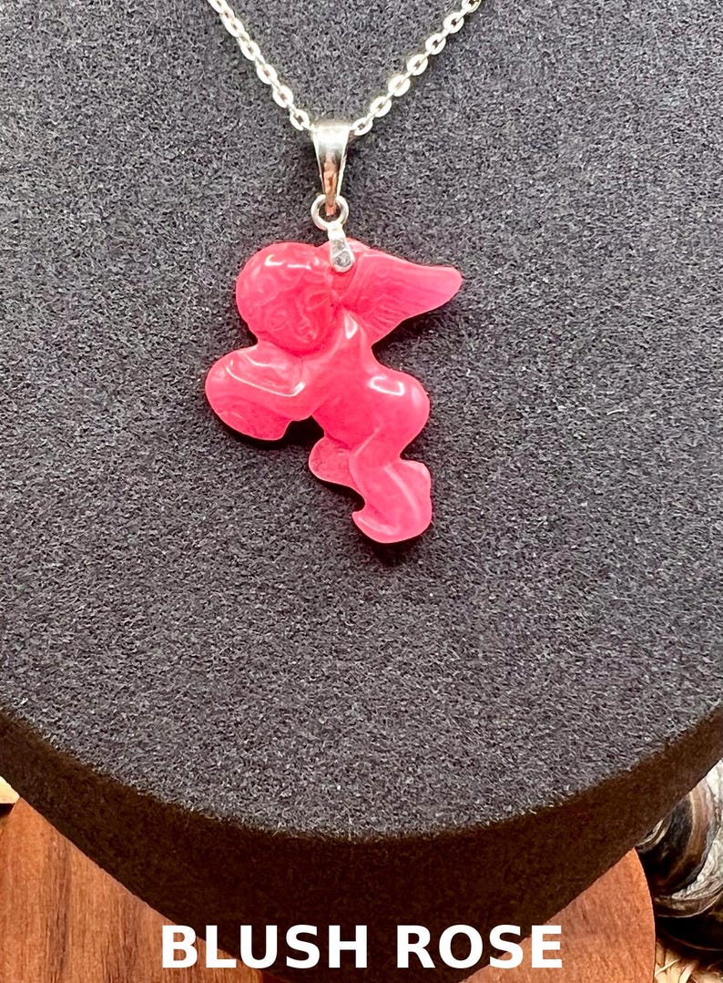 Puede incluir: Collar con colgante rosa y cadena plateada. El colgante tiene una forma abstracta y un acabado liso. El texto "BLUSH ROSE" est&aacute; en la parte inferior de la imagen.