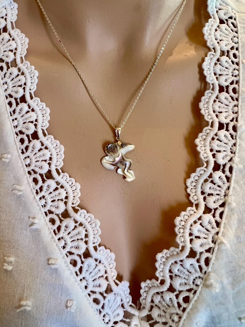 Puede incluir: Un collar con colgante de plata con un dise&ntilde;o abstracto. El colgante cuelga de una fina cadena de plata. El collar se muestra sobre una blusa blanca con detalles de encaje.