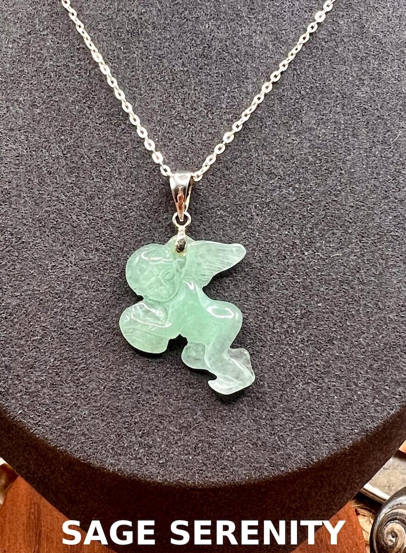 Puede incluir: Un collar de cadena plateada con un colgante que representa un &aacute;ngel tallado en verde claro. El colgante tiene forma de querub&iacute;n con alas. El texto "SAGE SERENITY" est&aacute; en la parte inferior de la imagen.
