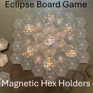 以下が含まれることがあります： Eclipseボードゲームとマグネット六角ホルダー。ゲームボードは、銀河のデザインの六角形のタイルで構成されています。タイルは、大きなプレイエリアを形成するように配置されています。「Eclipse Board Game」と「Magnetic Hex Holders」の文字が見えます。
