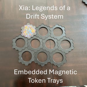 May include: Black gear-shaped token trays with a colorful game token. The text "Xia: Legends of a Drift System" and "Embedded Magnetic Token Trays" are displayed on the image. The trays are designed to hold game tokens.