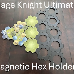 Pode incluir: Imagem de suportes hexagonais magnéticos pretos e peças de jogo. O texto "Mage Knight Ultimate" e "Magnetic Hex Holders" é exibido. As peças do jogo apresentam um design de paisagem com cores verdes, azuis e castanhas. Para jogos de tabuleiro.