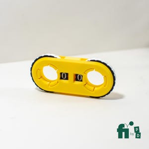May include: A yellow counter with black and white wheels and two circular openings. The counter displays "00" in black. The product is on a white surface.