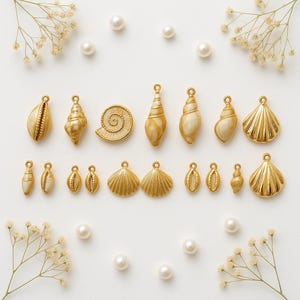 Puede incluir: Una colección de colgantes y dijes dorados con forma de concha marina en varias formas y tamaños, incluyendo conchas, vieiras y diseños en espiral. Los dijes están dispuestos sobre una superficie blanca con perlas dispersas y delicadas flores blancas.